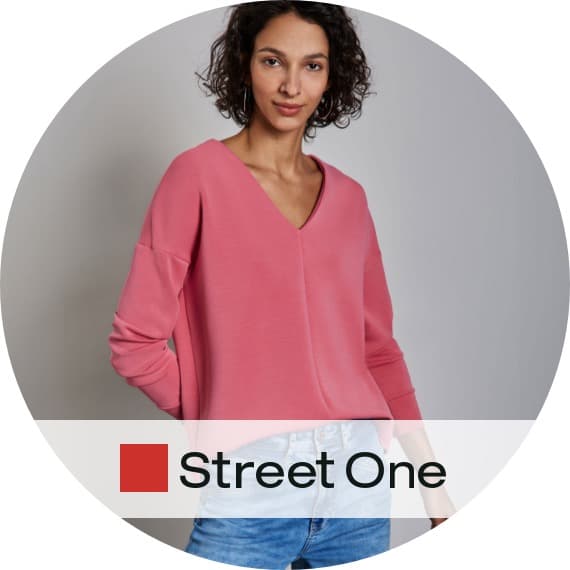 Street One – Person trägt rosa V-Ausschnitt-Pullover zu hellblauer Jeans, Hände in den Hosentaschen