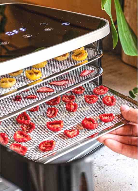 Digitale Anzeige mit Schriftzug OFF, darunter Dörrgerät mit Gittern voller Tomaten- und Bananenscheiben in der Küche