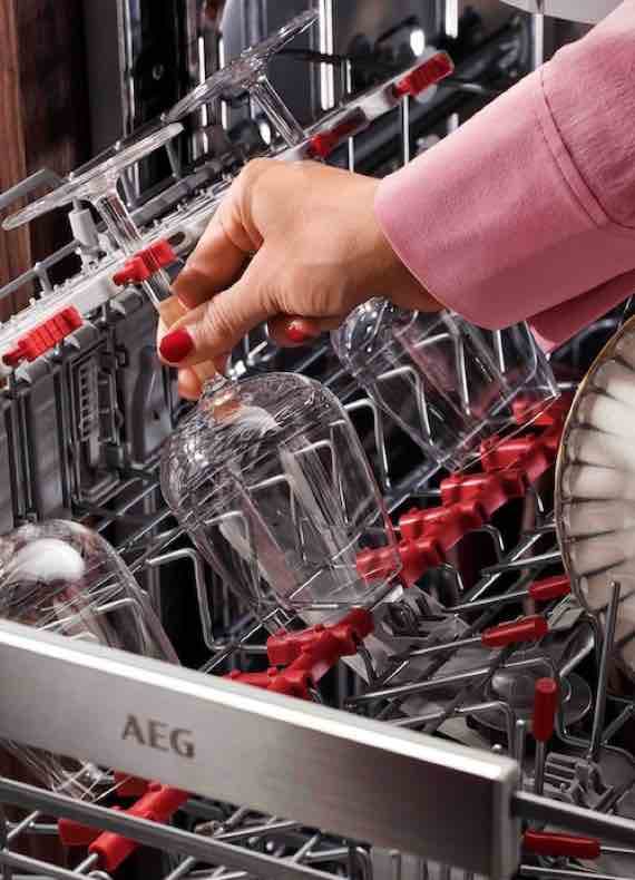 Hand stellt Weinglas kopfüber in den unteren Korb einer AEG Spülmaschine mit roten Halterungen