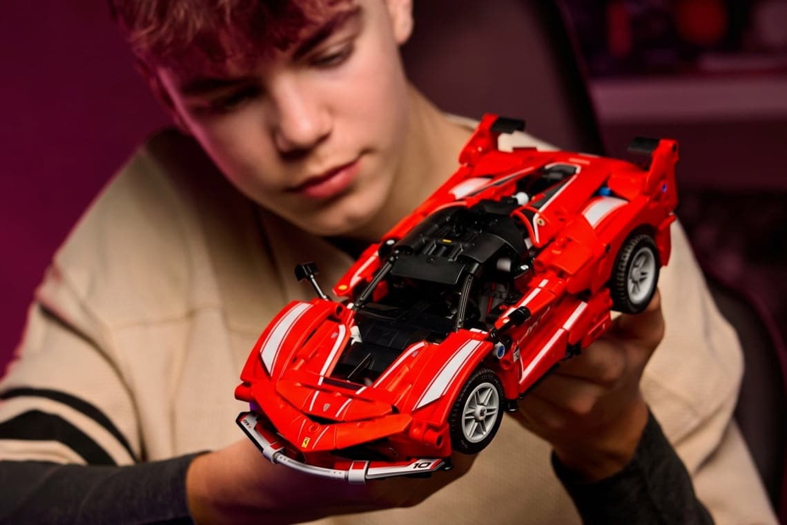 Jugendlicher hält ein großes rotes Spielzeug-Sportauto aus Bausteinen mit weißen Streifen in beiden Händen