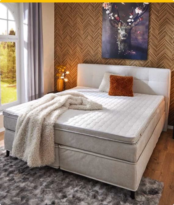 Gemütliches Schlafzimmer mit Doppelbett, weißer Tagesdecke und Kissen, buntes Bild an der Wand