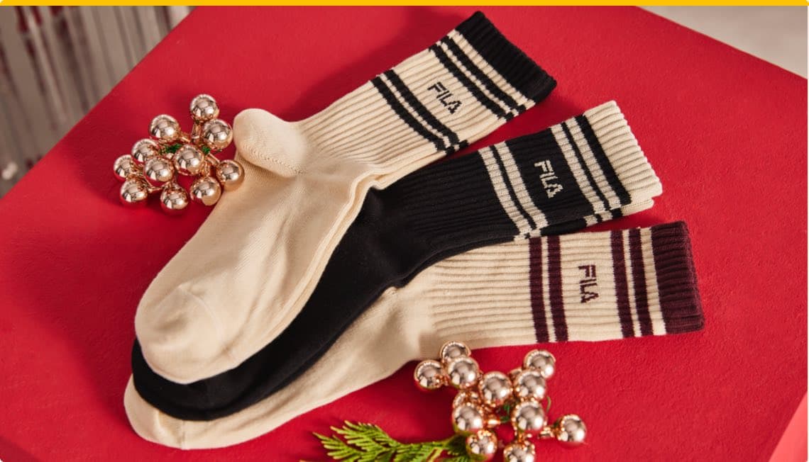 Socken in schwarz und beige auf rotem Untergrund mit Weihnachtsdekoration aus silbernen Kugeln und grünem Zweig