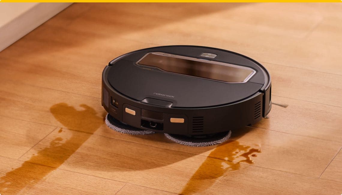 Schwarzer Saugroboter wischt Flüssigkeit auf einem Holzboden