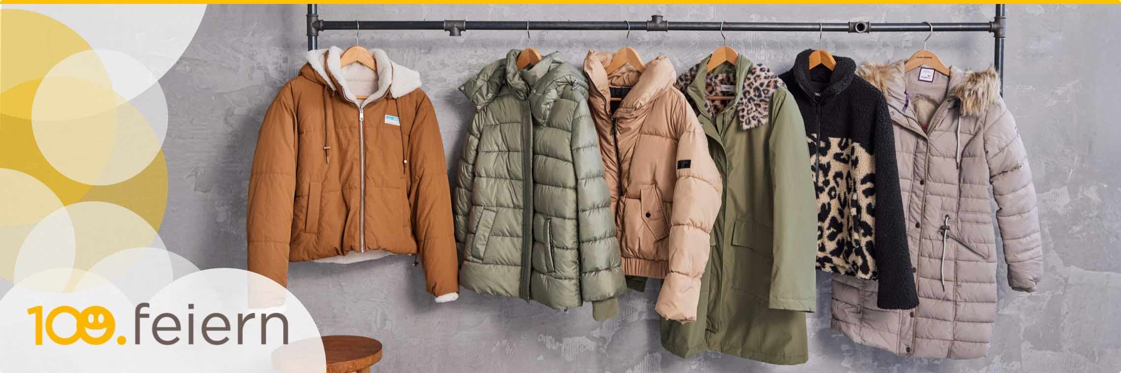 100. feiern – Sechs Winterjacken in verschiedenen Farben und Stilen hängen nebeneinander an einer Stange.