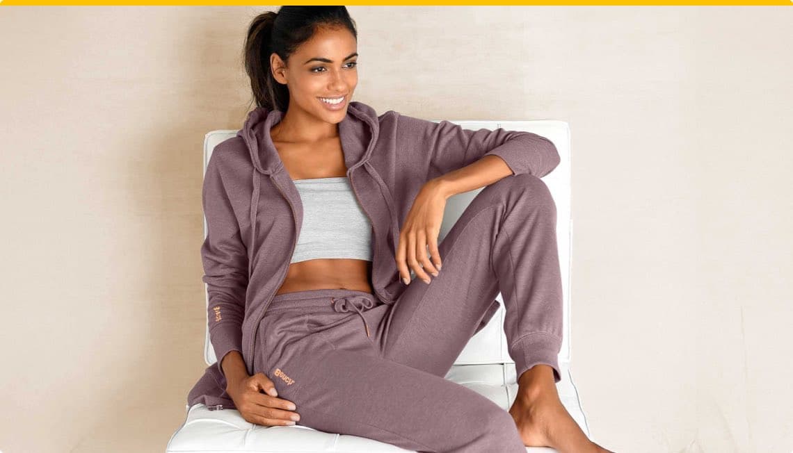 Frau sitzt in lila Jogginganzug und grauem Top auf weißem Stuhl, Gesicht unscharf