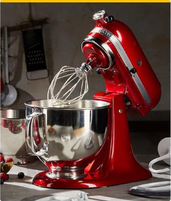 Rote Küchenmaschine mit Schneebesen und silberner Rührschüssel auf einer Küchentheke, im Hintergrund Küchenutensilien