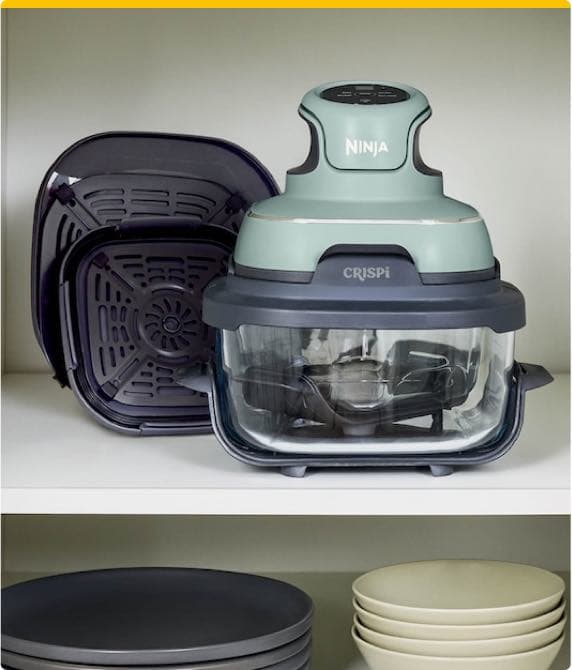 Ninja CRISPi Luftfritteuse steht auf einem Regal, daneben liegt der herausnehmbare Einsatz, darunter gestapelte Teller.