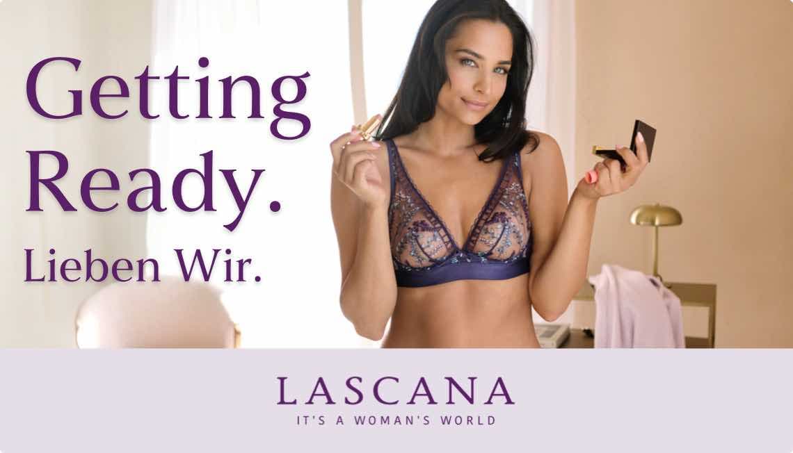 Getting Ready. Lieben Wir. Frau in lila Spitzen-BH trägt Lippenstift auf und hält einen Spiegel. LASCANA - It's a woman's world.