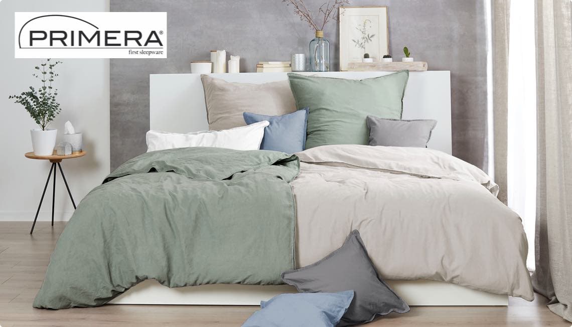 PRIMERA – modern eingerichtetes Schlafzimmer mit grauer, grüner und beiger Bettwäsche, Kissen und Dekor auf dem Bett und Regal.