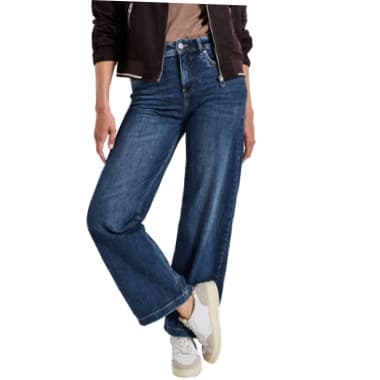 Frau trägt weite Jeans und Sneakers, hält eine Hand in der Tasche und steht locker mit überkreuzten Beinen.