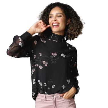 Frau in schwarzer Bluse mit Blumenmuster und rosa Hose hebt die Hand zum Kopf