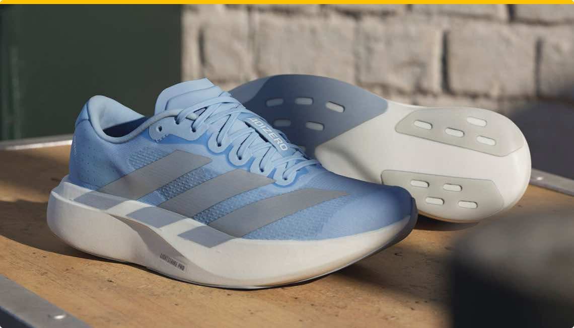 Hellblaue Laufschuhe mit weißen Sohlen und silbernen Streifen, seitliche und untere Ansicht auf Holztisch.