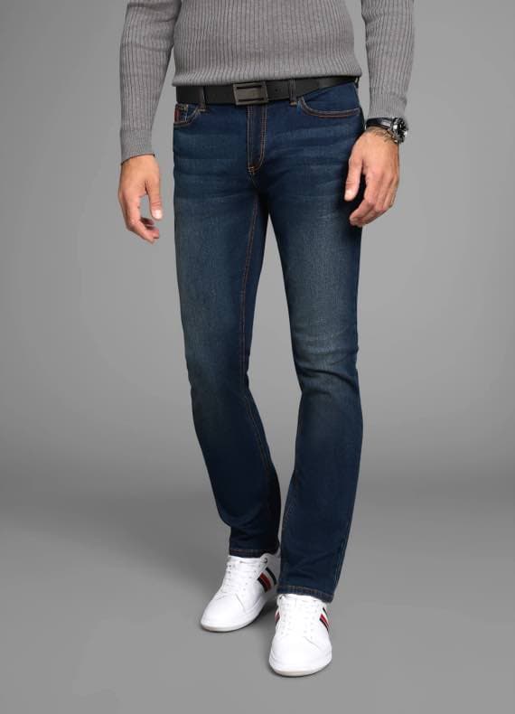 Mann in dunkelblauer Jeans und grauem Pullover, trägt weiße Sneakers mit roten und schwarzen Streifen, grauer Hintergrund