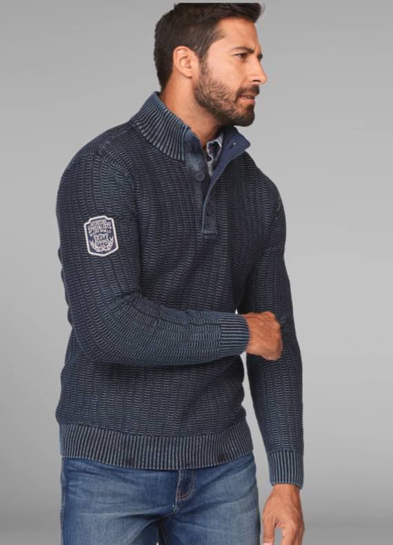 Mann in dunkelblauem Strickpullover mit Kragen und Knöpfen, Patch auf dem Ärmel, trägt blaue Jeans