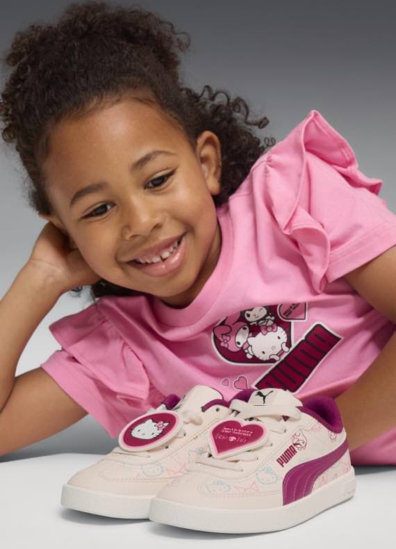 Mädchen in rosa Shirt, Hello Kitty Puma Turnschuhe vorne, Hello Kitty Grafik auf Shirt.