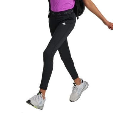 Frau in schwarzen Leggings und weißen Sneakers geht mit Schwung, trägt einen schwarzen Rucksack und ein lila T-Shirt.