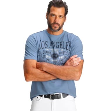 Mann in blauem T-Shirt mit "Los Angeles" Aufdruck, verschränkt die Arme vor weißem Hintergrund.
