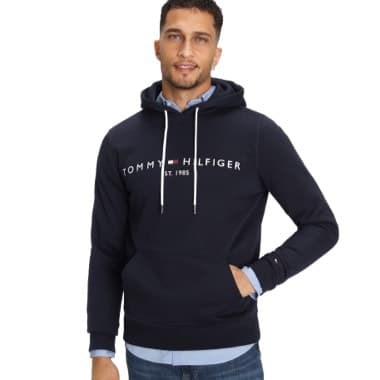 Schwarzes Tommy Hilfiger Hoodie mit weißem Schriftzug, Mann hat eine Hand in der Tasche und trägt ein blaues Hemd darunter