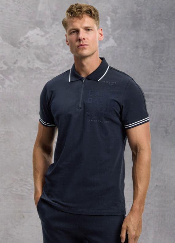 Mann in dunkelblauem Poloshirt mit Reißverschluss und gestreiften Ärmelabschlüssen vor grauem Hintergrund.