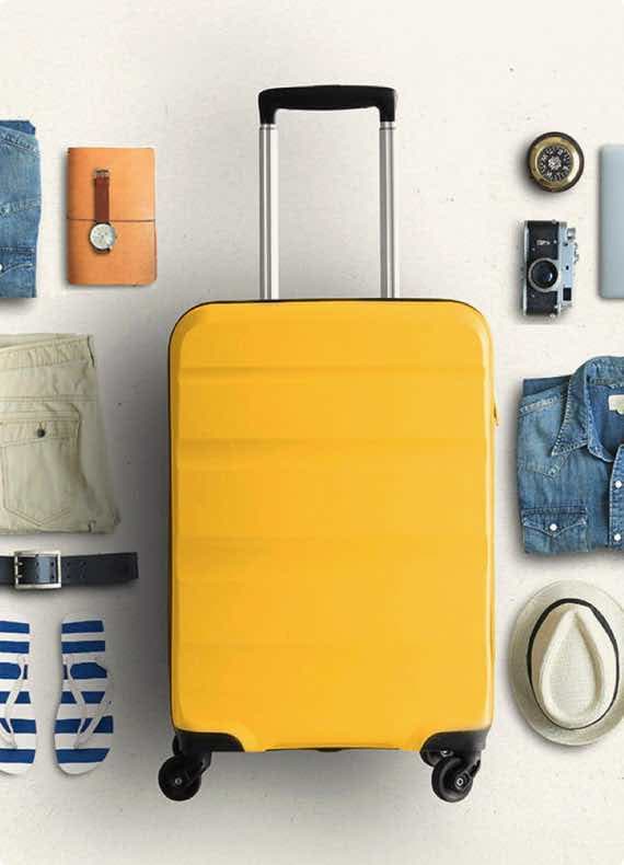 Gelber Rollkoffer neben Reisekamera, Hut, Kleidung und Accessoires auf hellem Hintergrund