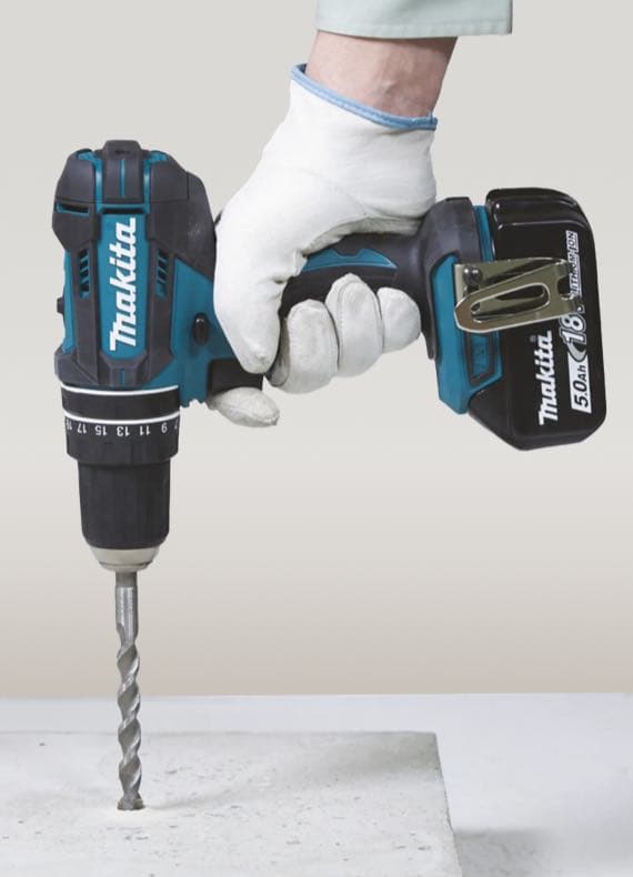 Akkubohrer von Makita wird von einer behandschuhten Hand gehalten und bohrt in Beton.