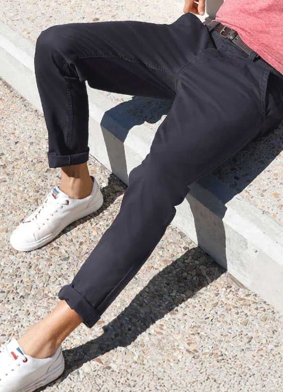 Mann sitzt auf Betonstufe, trägt schwarze Chino mit umgeschlagenem Saum, weißen Sneakern und rotes T‑Shirt