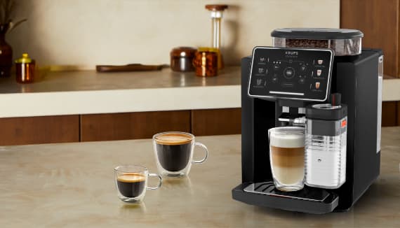Vollautomat in moderner Küche bereitet Latte Macchiato zu, daneben zwei Tassen Kaffee auf der Arbeitsplatte
