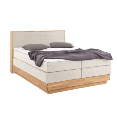 Doppelbett mit hellem Kopfteil, zwei Kissen und locker ausgebreiteter Decke auf erhöhtem Bettgestell