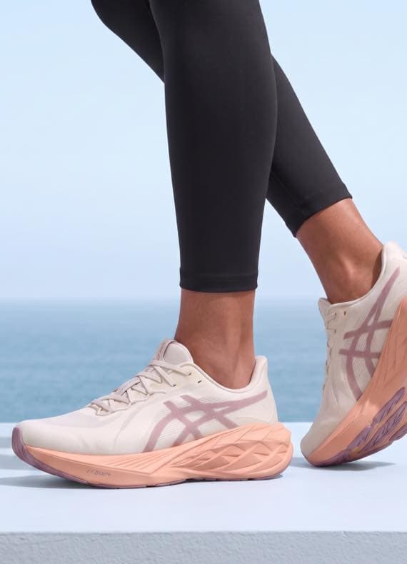 Füße in hellen Laufschuhen mit rosa Sohle, Person in schwarzen Leggings steht vor Meereshorizont