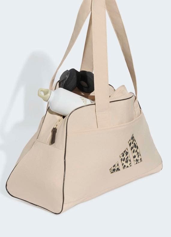 Beige Sporttasche mit seitlichem Logo in Leopardenmuster, gefüllt mit Handtuch, Kopfhörern und weißer Trinkflasche