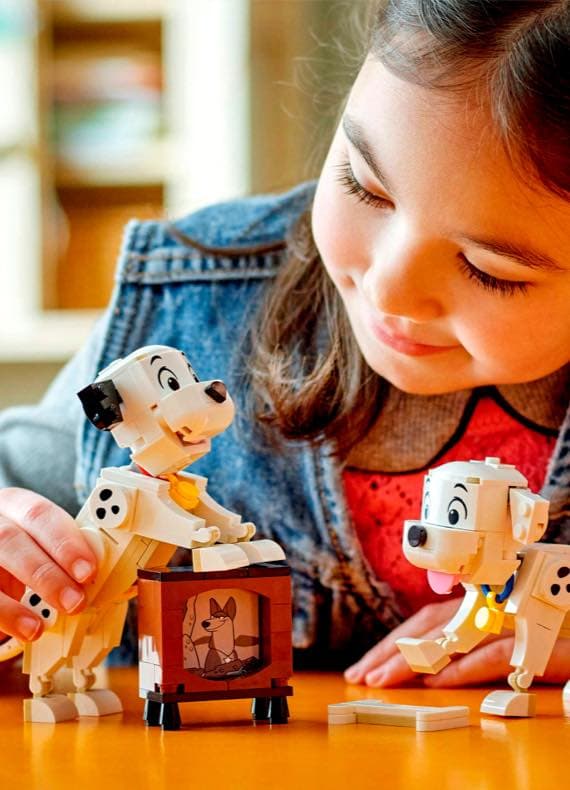 Kind spielt am Tisch mit weißen Dalmatiner-Bauspielzeugen und kleinem Fernseher mit Hundezeichnung