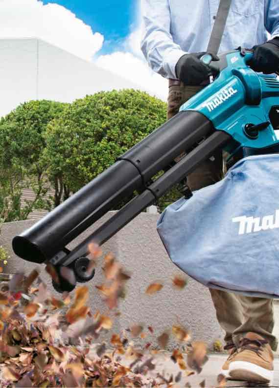 Person arbeitet im Garten mit Laubsauger, der herabgefallene Blätter einsaugt und in einen Auffangsack leitet