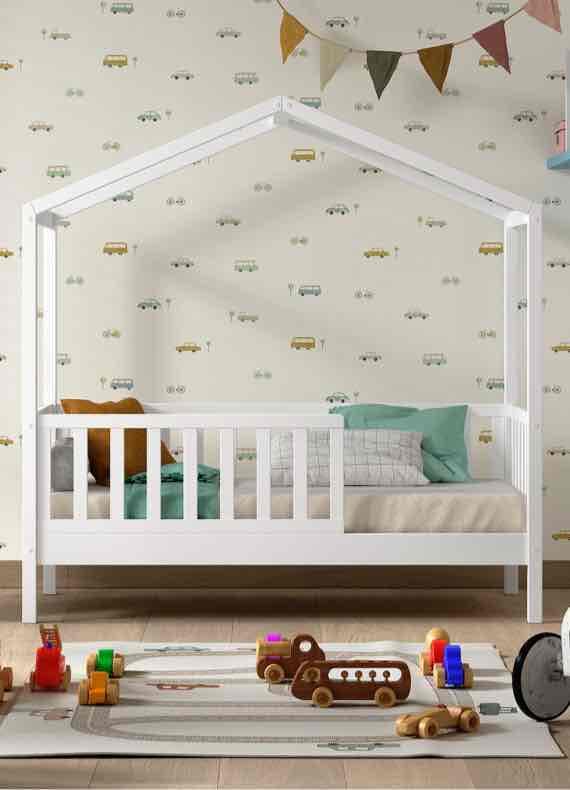 Weißes Kinderhausbett mit Kissen, davor Spielteppich mit Holzautos in einem hellen Kinderzimmer
