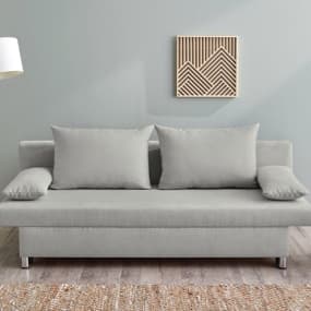 Ein modernes, graues Sofa mit zwei großen Kissen, das vor einer hellen Wand steht. Über dem Sofa hängt ein geometrisches Wandbild, und der Boden ist mit einem warmen Teppich bedeckt. Eine Stehlampe ergänzt die gemütliche Atmosphäre des Raumes.