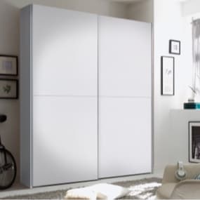 Ein moderner, weißer Kleiderschrank mit glatten Türen, der in einem hellen Raum steht. Um den Schrank herum sind einige Bilderrahmen an der Wand angebracht, und im Vordergrund liegt ein weicher Teppich.