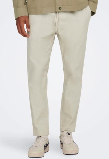 Eine Person trägt helle, lässige Stoffhosen mit einem entspannten Schnitt. Dazu kombiniert sie weiße Sneakers, die einen sportlichen Akzent setzen. Die Oberbekleidung ist in einem neutralen Farbton gehalten und ergänzt das Outfit.