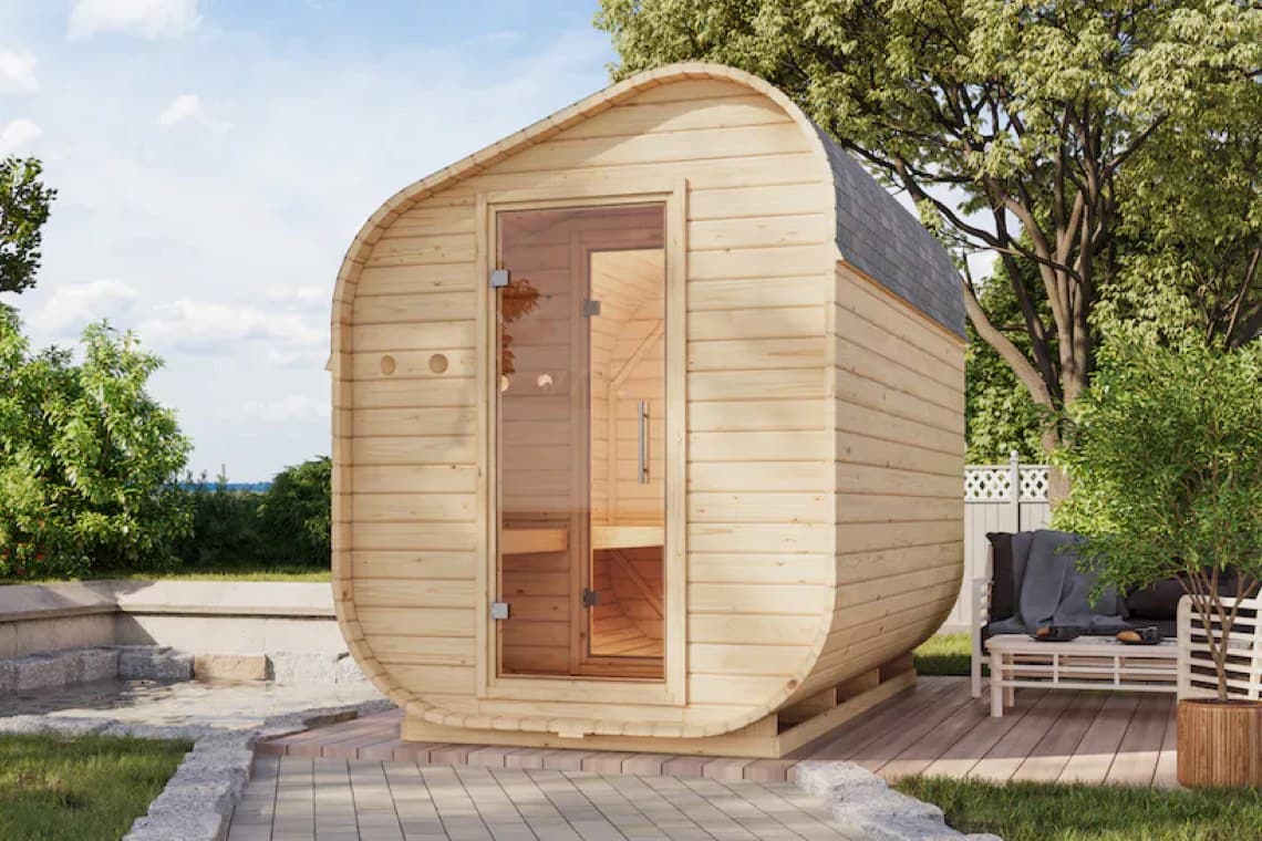 Holzsauna mit gewölbtem Dach, Glastür auf Holzterrasse, umgeben von Bäumen
