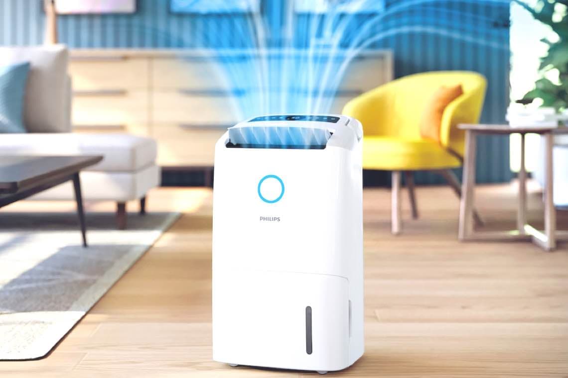 Weißer Luftreiniger von Philips in einem modernen Raum, blauer Lichtkreis oben, Holzfußboden, gelber Stuhl im Hintergrund.