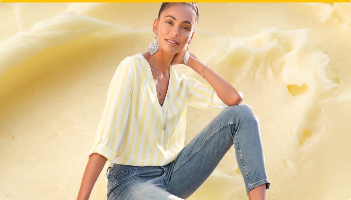 Modisches Angebot: Frau in gestreiftem Shirt und Jeans posiert vor einem hellen, cremigen Hintergrund.