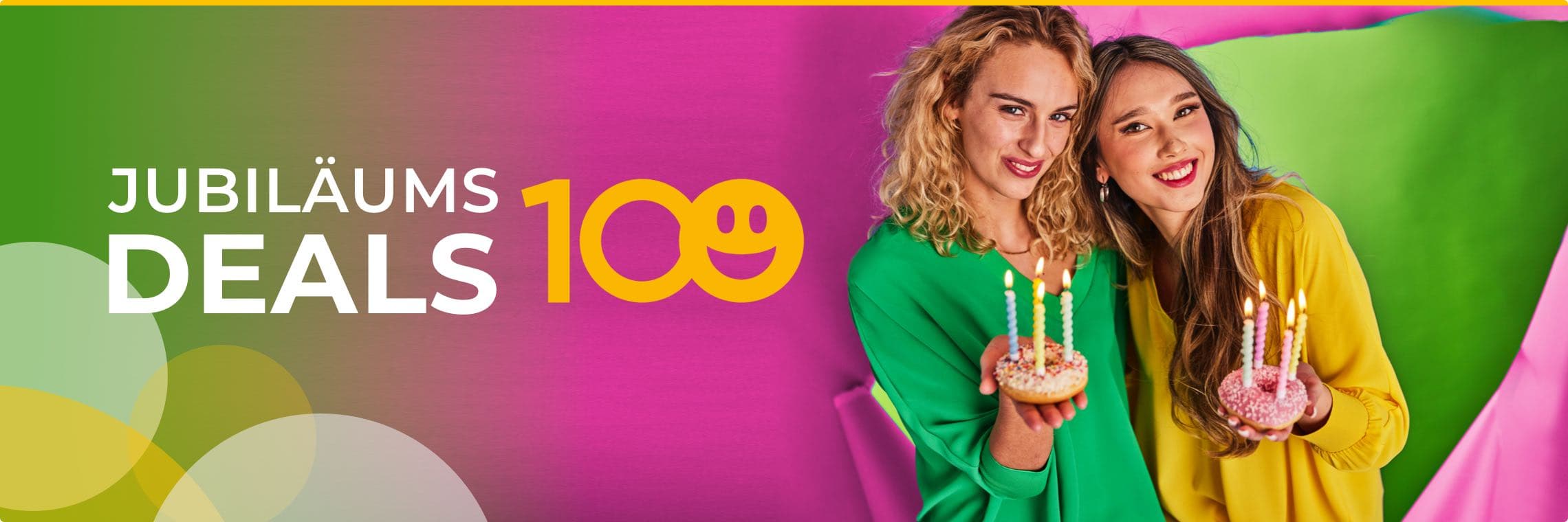 Jubiläums Deals 100 – Zwei Frauen in bunten Oberteilen halten verzierte Donuts mit Kerzen vor einem farbenfrohen Hintergrund