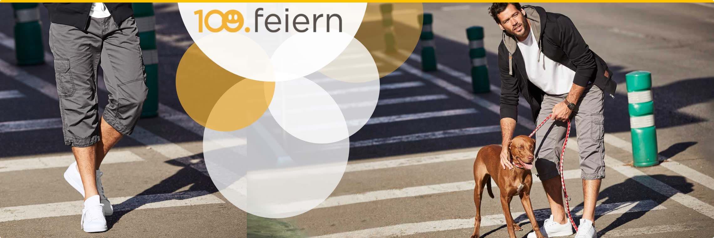 100. feiern – Mann mit Hund an der Leine überquert die Straße in grauen Cargo-Shorts und weißen Sneakers