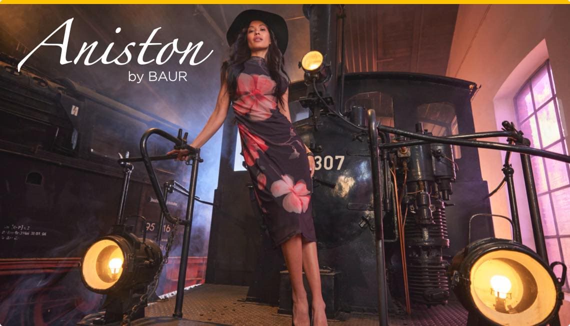 Aniston by BAUR – Frau in langem Kleid mit Blumenmuster steht auf einer alten Dampflok
