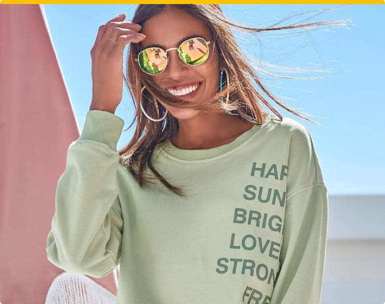 Frau mit Sonnenbrille trägt Langarmshirt mit Schriftzug "HAPPY SUN BRIGHT LOVE STRONG FREE"