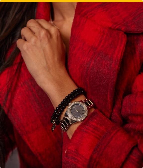 Frau in rotem Mantel trägt silberfarbene Armbanduhr und schwarze Perlenarmbänder am Handgelenk