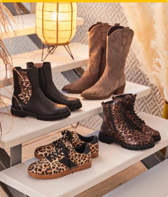 Vier Paar Damenstiefel und Schuhe mit Leopardenmuster auf weißen Regalen, darunter Chelsea Boots, Cowboystiefel und Sneaker