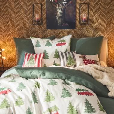 Weihnachtlich dekoriertes Schlafzimmer mit Bettwäsche, die Weihnachtsbäume und rote Autos zeigt, Wandbild eines Hirschs über dem Bett