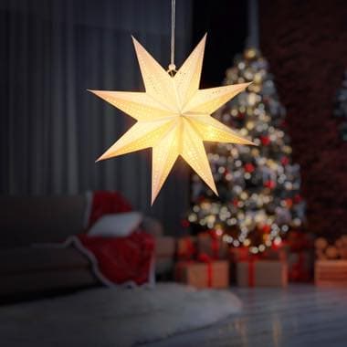 Leuchtender Weihnachtsstern hängt vor geschmücktem Weihnachtsbaum, Sofa mit roter Decke und Geschenke im Hintergrund