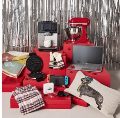 Verschiedene Geschenke auf roten Boxen: Laptop, Mixer, Waffeleisen, Konsole, Kopfhörer, Tassen, Kissen und Kleidung vor silbernem Hintergrund