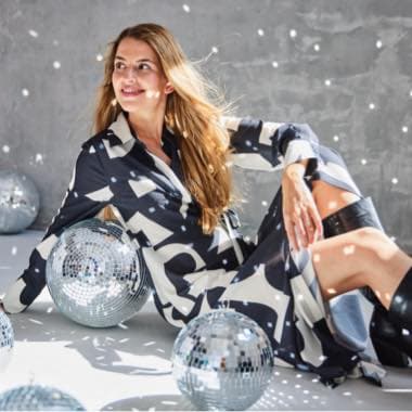 Frau in gemustertem Kleid sitzt umgeben von Diskokugeln