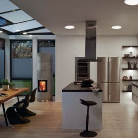 Moderne Küche mit Esstisch, Kaminofen, Edelstahlgeräten und Kochinsel in hellem Raum mit großen Fenstern.